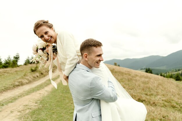 Lo sposo allegro tiene una bella sposa tra le braccia giovani coppie felici che giocano e si concedono il giorno delle nozze