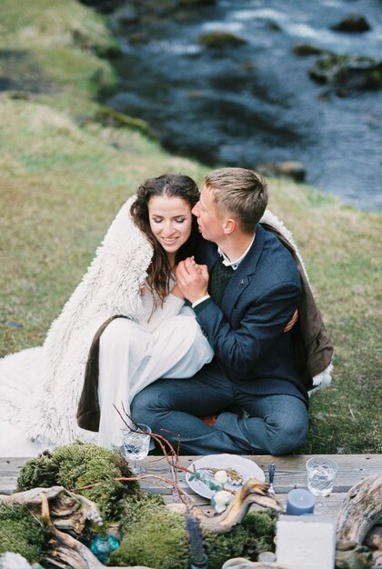 Lo sposo bacia la sposa in una coperta alla tavola imbandita sulla riva del fiume