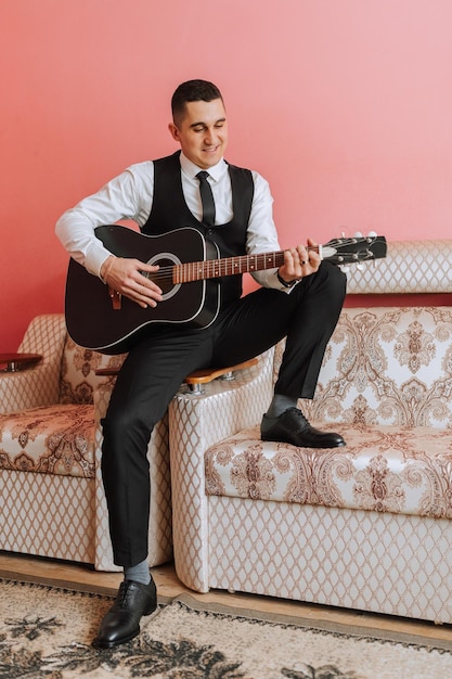 Lo sposo canta canzoni alla chitarra al mattino nella sua stanza sposo in abito nero uomo felice preparazione per il matrimonio