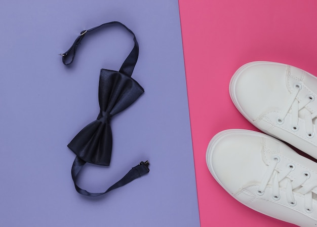 Lo sposo di natura morta di moda minimalista guarda Eleganti scarpe da ginnastica bianche e un papillon su sfondo rosa viola