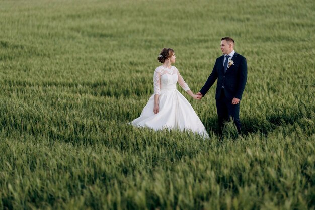 Lo sposo e la sposa camminano lungo il campo di grano verde in una giornata luminosa