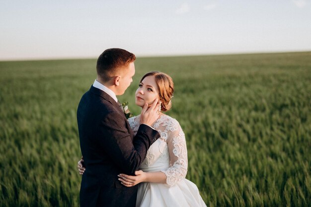 Lo sposo e la sposa camminano lungo il campo di grano verde in una giornata luminosa