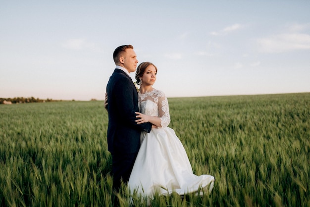Lo sposo e la sposa camminano lungo il campo di grano verde in una giornata luminosa