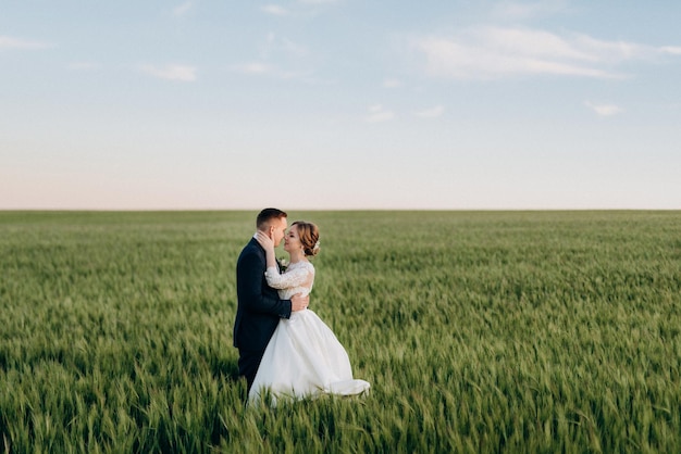 Lo sposo e la sposa camminano lungo il campo di grano verde in una giornata luminosa