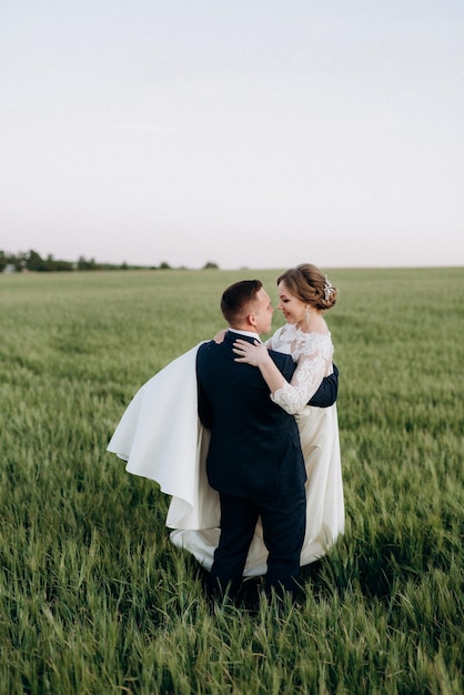 Lo sposo e la sposa camminano lungo il campo di grano verde in una giornata luminosa