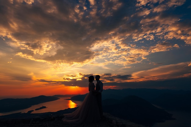 Lo sposo e la sposa stanno sulla montagna sullo sfondo del tramonto