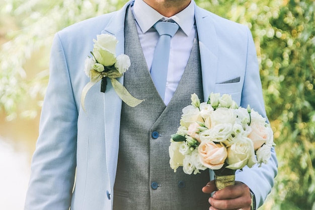 Lo sposo in abito blu è in piedi all'aperto Bell'uomo tiene in mano il bouquet da sposa
