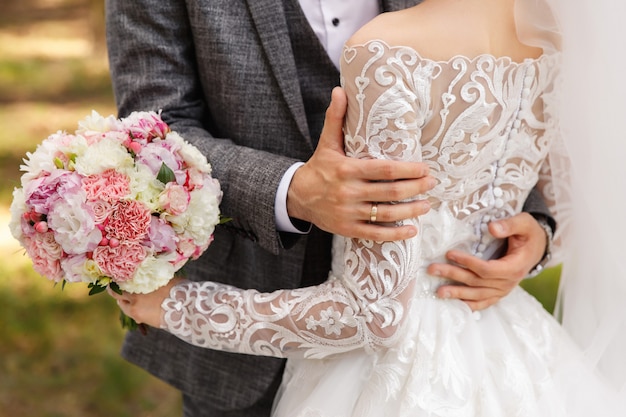 Lo sposo in abito grigio abbraccia la sposa in abito da sposa con maniche lunghe