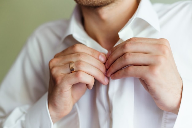 Lo sposo in camicia bianca allaccia i bottoni. Primo piano della riunione dello sposo.