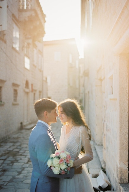 Lo sposo quasi bacia la sposa con un bouquet in una stradina di una città vecchia