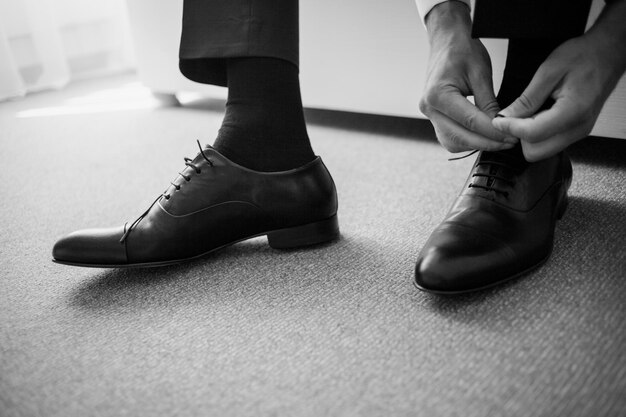 Lo sposo seduto sul divano e legato i lacci delle scarpe su scarpe di pelle nera. foto in bianco e nero