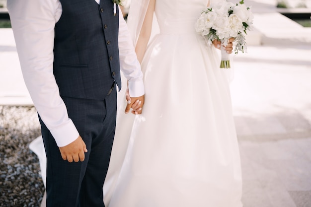 Lo sposo tiene la mano della sposa in un abito bianco con un mazzo di fiori