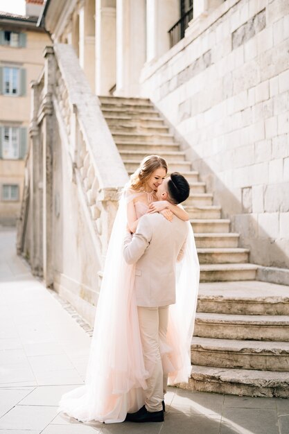 Lo sposo tiene la sposa tra le braccia vicino ai gradini di un vecchio edificio a bergamo italia