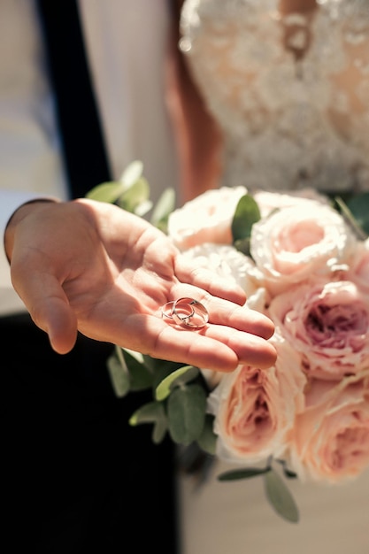 Lo sposo tiene le fedi nuziali Sullo sfondo la sposa tiene un bouquet Giornata di sole