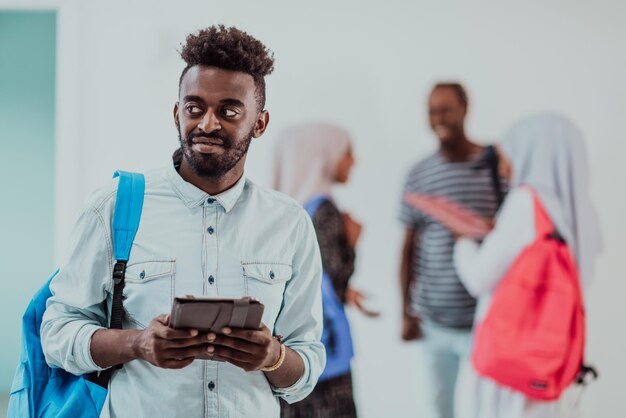 Lo stile di vita dell'università Il bel giovane studente che tiene un tablet e sorride mentre è in piedi contro l'università con i suoi amici ha una riunione di squadra sullo sfondo. Foto di alta qualità. Alto