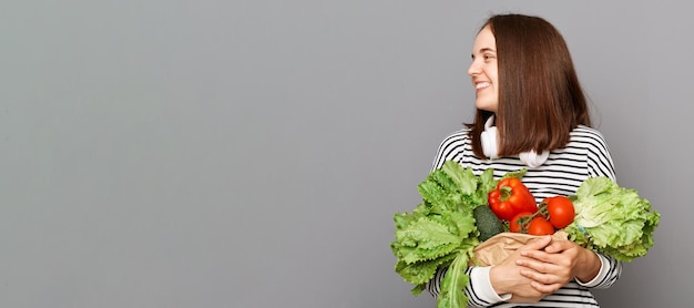 Lo stile di vita vegetariano nutre e prospera Chiave fresca e biologica per il benessere alimentata da cibo nutriente Donna gioiosa che tiene verdure isolate su sfondo grigio copia spazio per la pubblicità