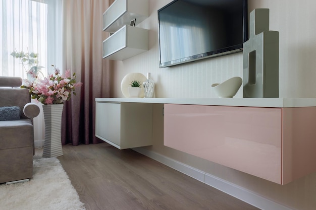 Lo stile moderno del soggiorno nei colori rosa e bianco con armadio e TV