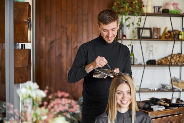 Lo stilista maschio sicuro sta tingendo i capelli del cliente femminile caucasico biondo