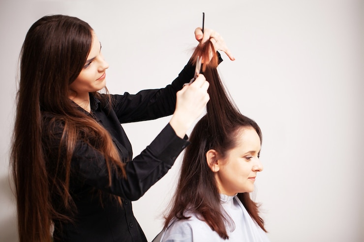 Foto lo stilista professionista rende una giovane donna una bella acconciatura.