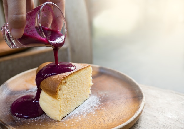 Lo strato della torta è superato con la salsa della frutta rossa su un piatto di legno.