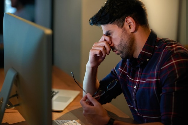 Lo stress di lavorare per lunghe ore Foto ritagliata di un giovane uomo d'affari che sembra stressato mentre lavora fino a tardi in un ufficio