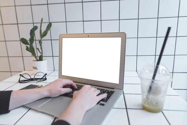 lo studente lavora su un laptop con uno schermo bianco nella caffetteria e beve un frullato.