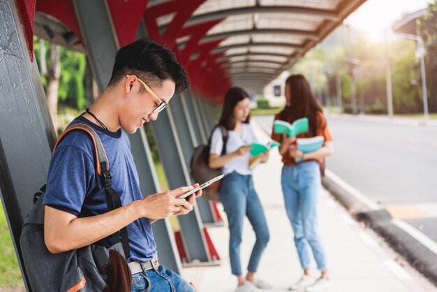 Lo studente maschio legge sul computer tablet al campus. Ci sono gruppi di amiche dietro, concetto di educazione