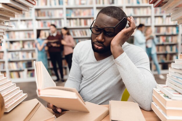 Lo studente studia in biblioteca annoiato e stanco.