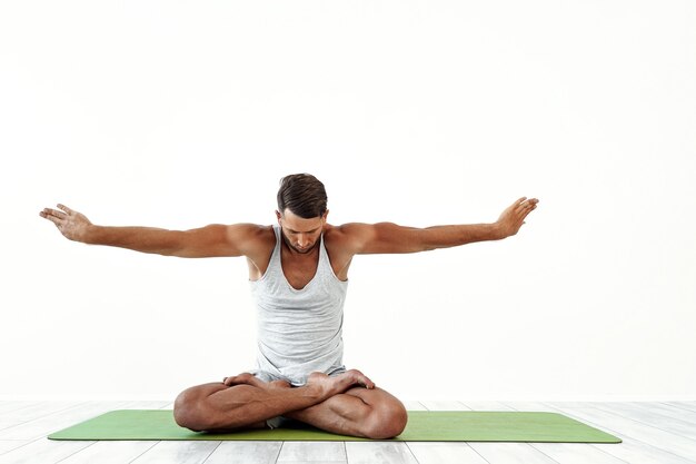 Lo yoga maschile medita in posa classica in studio su bianco