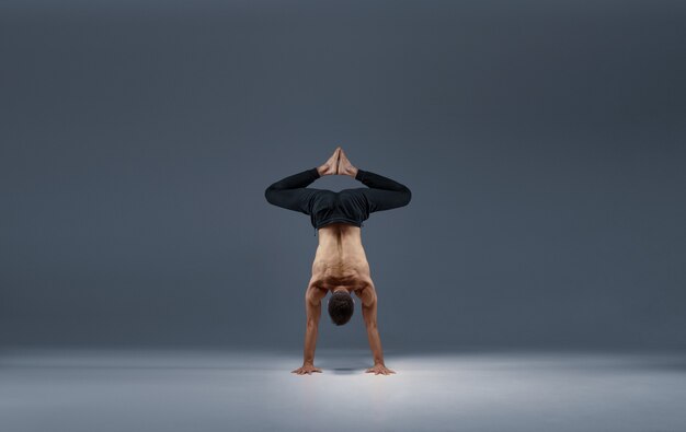 Lo yoga maschile si divide sulle mani, vista posteriore, muro grigio Uomo forte che fa esercizio yogi, allenamento asana, massima concentrazione, stile di vita sano