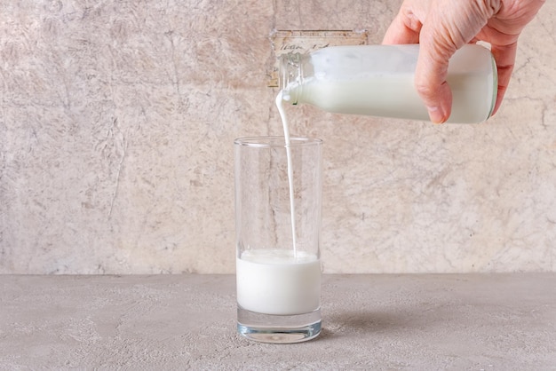 Lo yogurt viene versato da una bottiglia in un bicchiere su uno spazio di copia di sfondo beige