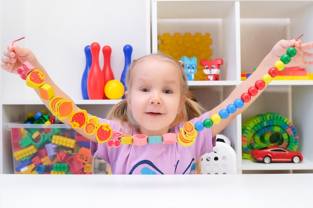 Logopedia, lo sviluppo delle capacità motorie. La ragazza del bambino sta infilando le perline su una corda.