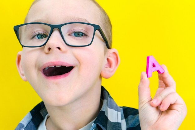 Logoterapia. Il bambino dice la lettera A. Lezioni con un logopedista. ragazzo su sfondo giallo isolato