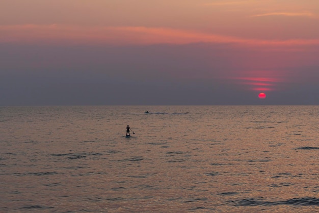Lonely SUP board man Surfer naviga in movimento sull'acqua di mare verso il tramonto delle avventure in mare
