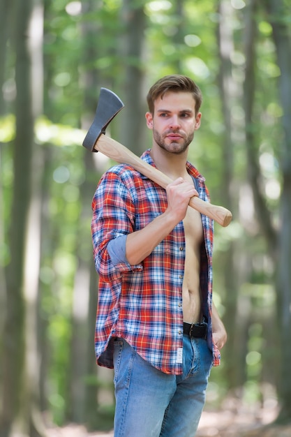 Look robusto L'uomo con la barba lunga porta l'ascia nei boschi L'uomo dell'ascia in stile boscaiolo indossa una camicia a quadri aperta