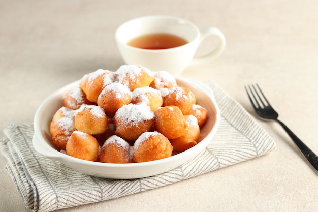 Loukoumades, luqaimat o lokma con copertura di zucchero semolato fine in un piatto bianco.