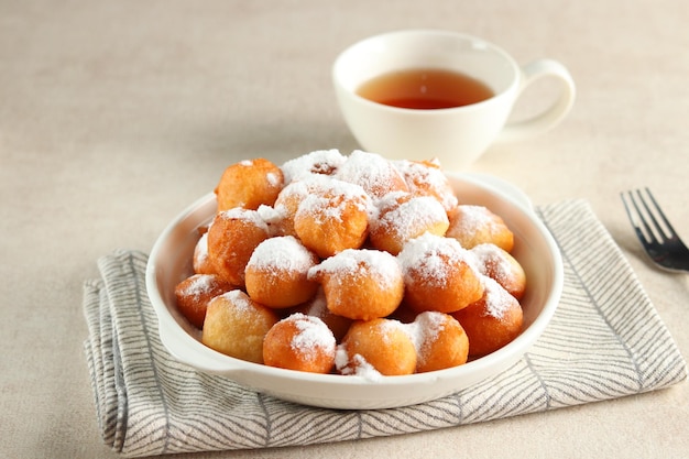 Loukoumades, luqaimat o lokma con copertura di zucchero semolato fine in un piatto bianco.