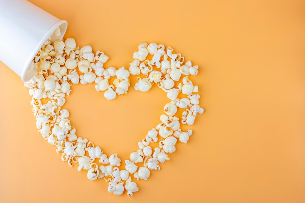 Love movies concept. Popcorn in paper box scattered on orange background heart shaped top view, copy space for text. Cinema snack concept. Popcorn box mocap