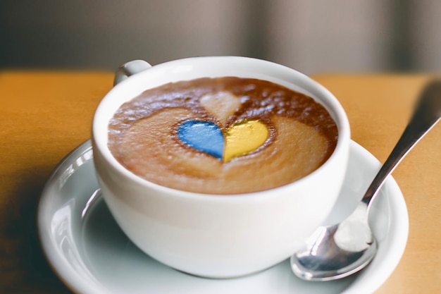 Love Ukraine Una tazza di caffè con un motivo della bandiera ucraina a forma di cuore sul tavolo Disegni patriottici