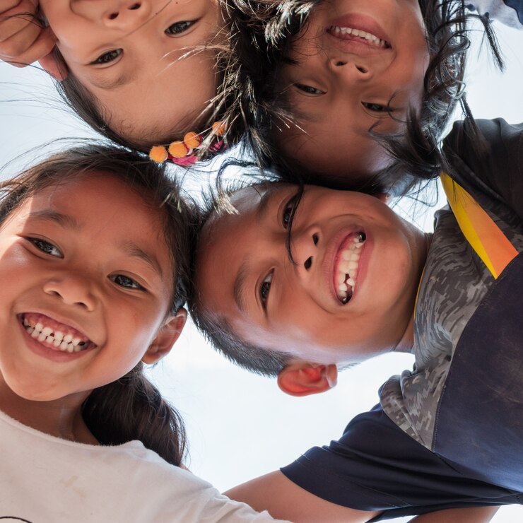 Low angle shot of excited children stand in circle hugging looking at camera at playing together, Team of smiling kids embracing together in a circle. Portrait of young boy and girls looking at camera