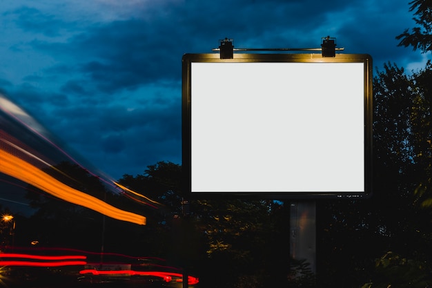 Luce di traccia sfocata vicino al cartellone bianco bianco per la pubblicità di notte