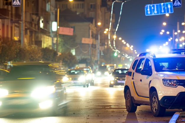 Luci blu lampeggianti luminose di un'auto di pattuglia della polizia parcheggiata in una strada cittadina con traffico notturno.