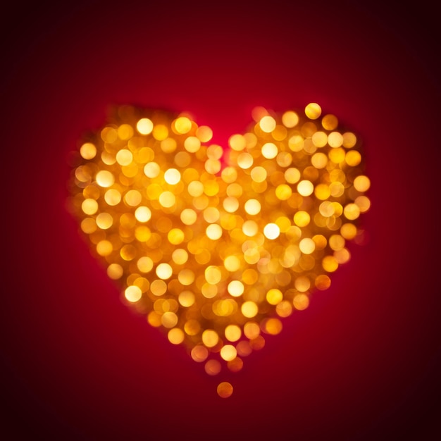 Luci bokeh color oro luccicanti sfocate a forma di cuore sullo sfondo rosso scuro