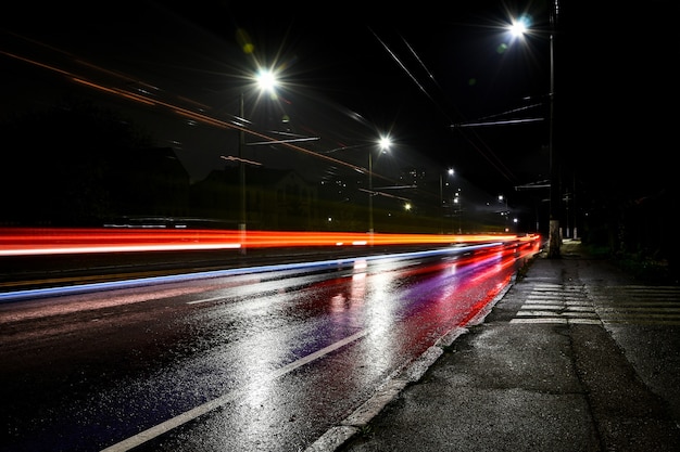 Luci delle auto di notte. Luci stradali. Città notturna. Strada notturna di fotografia a lunga esposizione. Fasce colorate di luce sulla strada. Strada bagnata dopo la pioggia.