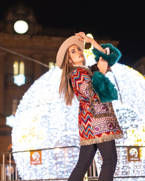 Luci di Natale in città, ragazza bionda caucasica appollaiata accanto a una palla gigante illuminata, stile di vita invernale