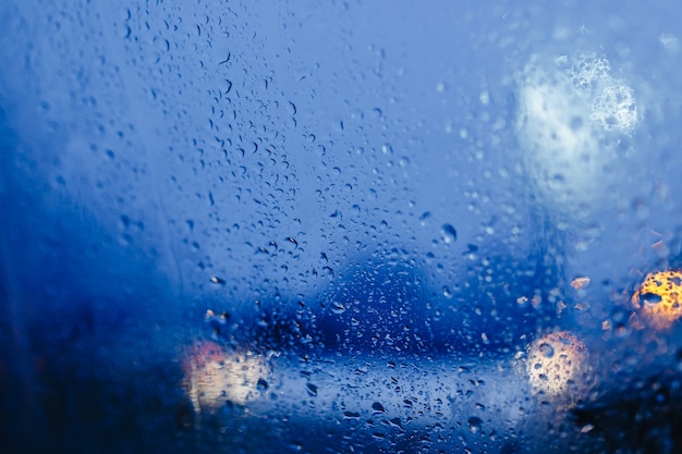 Luci notturne della città attraverso il parabrezza astratto goccia d'acqua sulle luci di vetro e pioggia.