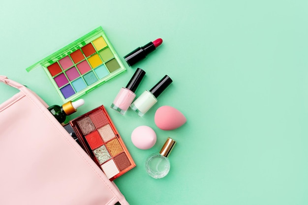 Luminosa palette di ombretti estivi e prodotti per il trucco in borsa cosmetica rosa su sfondo verde