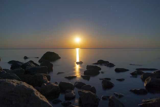 Luna piena sul mare di notte con un riflesso nell'acqua.