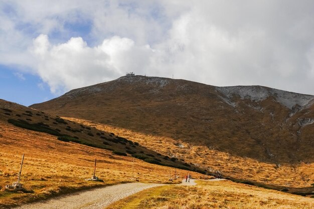 Lunga strada sterrata attraverso un paesaggio collinare con vista sulla vetta dalla montagna più alta