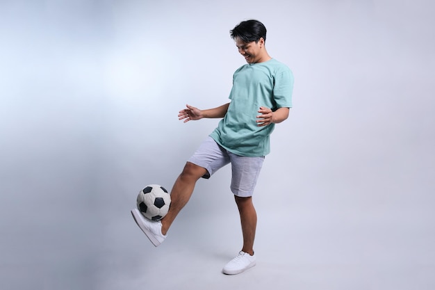 Lunghezza completa di un giocatore di calcio che gioca con una palla da calcio isolata su uno sfondo bianco